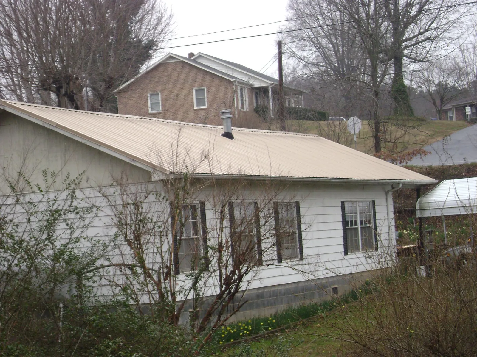 Tan metal roof on a white sided house set into a hillside — Commercial Roofing by Roofing Brothers in Bowman